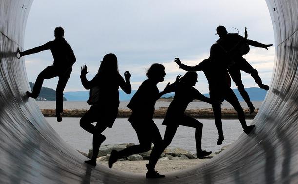 Blick aus einer Röhre auf den Strand. Es sind Schattenbilder von 6 Personen zu sehen, die sich in der Röhre bewegen.