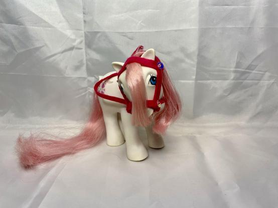 A toy pony with long pink hair and a red harness, positioned on a plain white background.