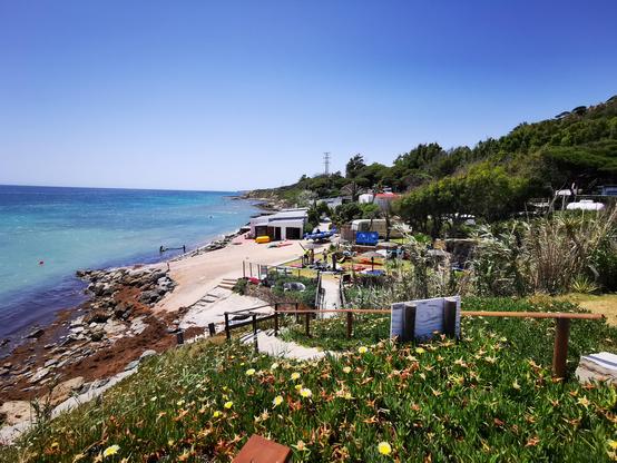 Blick vom Campingplatz auf den Strandzugang und die kleine Kneipe. Rechts ein Platz für Wassersportler