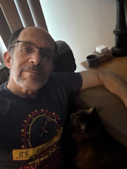 A man lounges with a smol brown tabby curled contentedly under his arm in a comfy armchair.