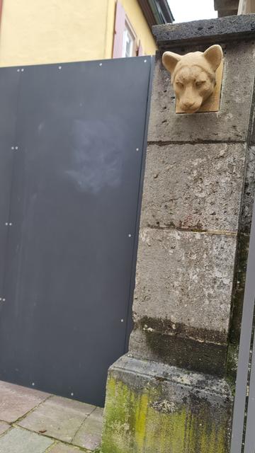 Zweimal, aus verschiedener perspektive, ein aus Sandstein gemeisselter katzenkopf an torpfosten befestigt, wie eine Art Wachkatze am Hauseingang?