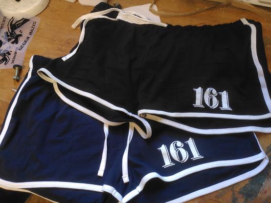 Zwei kurze sportshorts (schwarz bzw dunkelblau) mit weiß abgesetzten Nähten (n bisschen retro), auf dem linken Bein weißer Druck "161"