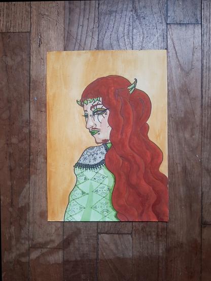 Peinture à l'aquarelle posée sur un parquet en bois.
On y voit un portrait d'une personne regardant par dessus son épaule.
Iel a les cheveux roux avec les pointes de sa frange vertes, iel a la peau blanche.
Iel fait la moue, ses piercings visibles sont placés en bas à gauche de sa bouche, au dessus de son sourcil, en dessous de sa bouche et au bridge de son nez.
Iel est maquilléx, les lèvres vertes, du far a paupière vert et marron,  un grand trait d'eyeliner noir et de longs cils stylisés.
Ses vêtements sont décorés, iel porte une longue cape verte claire ornementée de petites broderies avec des motifs géométriques et une épaulette grise avec des motifs de soleil et d'étoiles et bordée de dentelle.