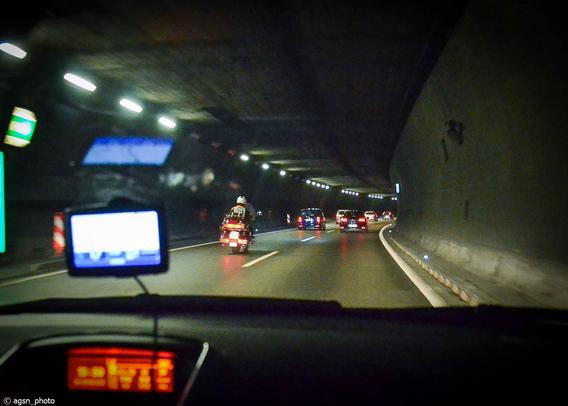 Blick vom Beifahrersitz eines Autos, das durch einen dunklen Tunnel fährt, mit anderen Autos und einem Motorrad davor. /
View from the passenger seat of a car driving through a dark tunnel with other cars and a motorcycle in front.