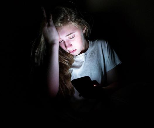 Jugendliche sitzt im Dunkeln und schaut besorgt auf ein Handy. Foto: Moore Media