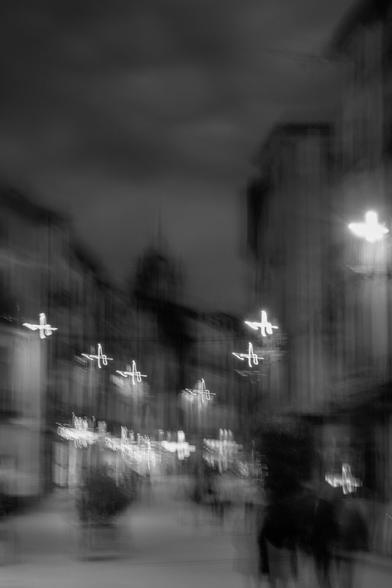 Vertical black and white photograph showing an urban scene abstracted by intentional camera movement.