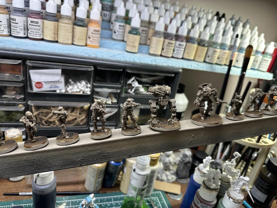 A long 1”x1” spray stick with BLKOUT Sci fi miniatures stuck on it, which have been sprayed tan and lightly washed brown.