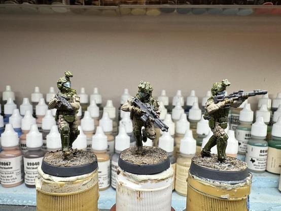 Three BLKOUT Task Force Boone miniatures with guns contrast painted dark blue grey, kit and armor in green, boots and gloves in dirty brown, with a metallic blue visor