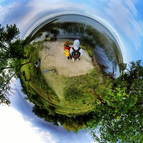 One of a series of photographs in which two people are pictured hiking, biking, and kayaking throughout a beautiful and verdant state park in central Minnesota under cloudy blue late-summer skies.