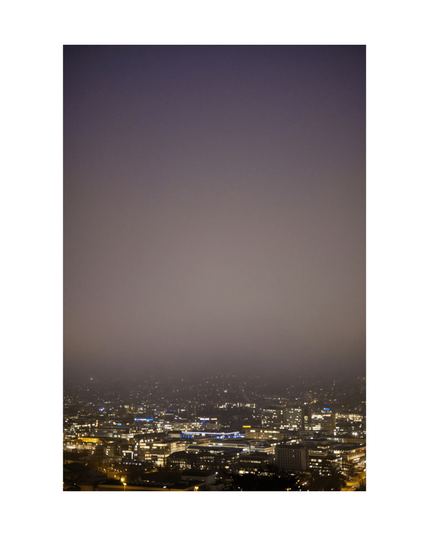 in the lower third a view over a city by night with white, blue and yellow lightdots, above is foggy air fading into smooth dark night light