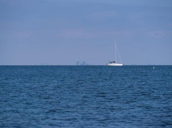A ship swimming in the Öresund and the Copenhagen skyline in the background. The sky is slightly blue.
