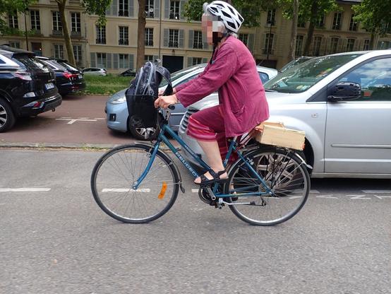 Cycliste en sandales sur un vélo Peugeot ancien avec un cageot sur le porte bagage