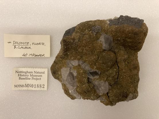 A specimen made up of a mixture of mineralss with two labels... it's light brown with white crystals...