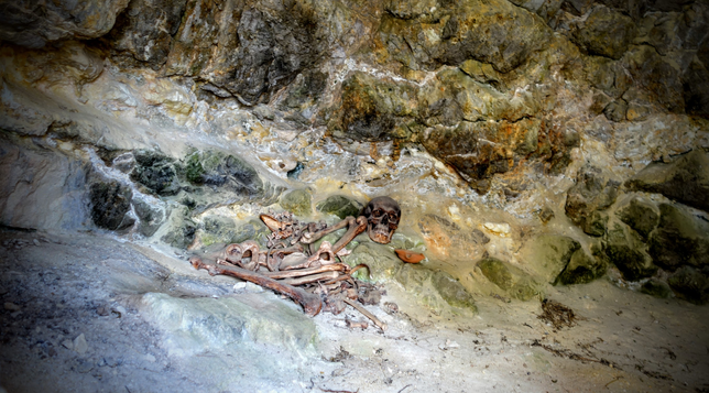In einer Höhle (alter Grabhügel) liegt ein Skelett zusammengesunken auf einem kleinen Felsvorsprung.