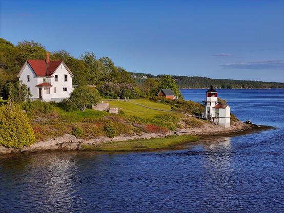 Squirrel Point Lighthouse from the north. A small white light tower sits on the shore below a white frame house.