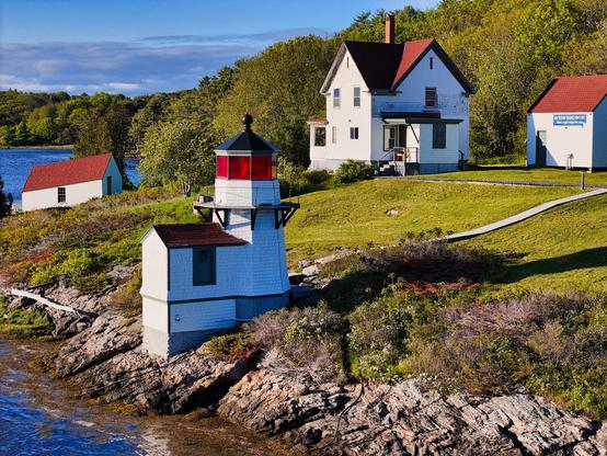 Squirrel Point Lighthouse from the southwest. A small white light tower sits on the shore below a white frame house, with a lifeboat boathouse in the background.