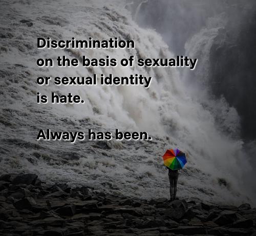 An image of a person standing next to a waterfall. The person is mostly hidden by an umbrella that resembles the colours of a rainbow, which typically is seen as a synonym for gay rights and LGBTQIA+ rights. Over that image, the following text is written: "Discrimination on the basis of sexuality or sexual identity is hate. Always has been."