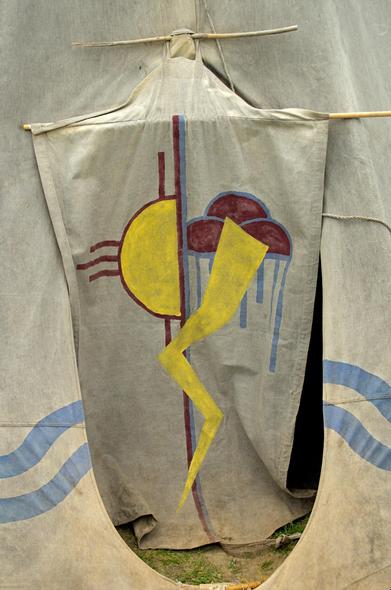 A door to a tipi with a sun and thunder cloud painted on it