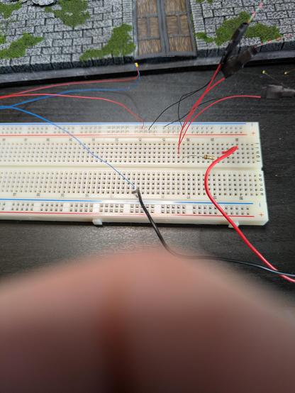 A solderless breadboard sits in front of the back panel of the diorama, on a table. A handful of tiny wires stick out with LEDs on their ends. A small flat battery pack is also connected.