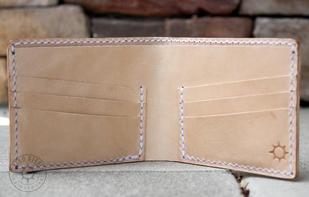 The interior of the wallet. It is solid natural leather with white stitching, and a makers mark in the bottom right corner