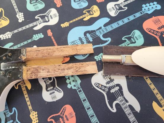 This picture shows the head of the guitar to the left and the part of the neck that it came away with.the part of the head you can see is black. The wood shows a bit of glue from the fingerboard. To the right is the end of the neck with the back of the rosewood fingerboard and the end of the truss rod visible.
Again, on the black bass desk mat I use for repairs.