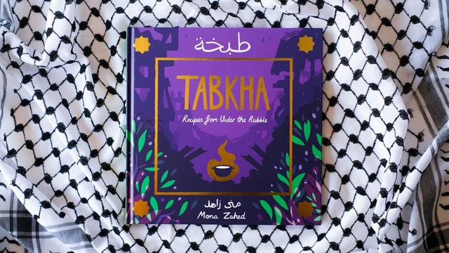 The purple cover the book "Tabkha" lies on a table covered by a Palestinian scarf.
