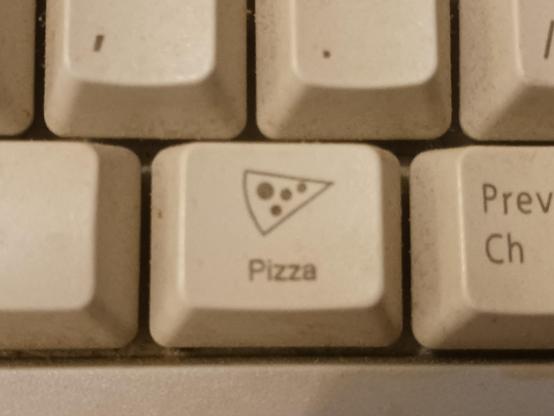 A close up shot of a pizza key on an old beige keyboard. The key has a pizza icon and the text "pizza" under it.