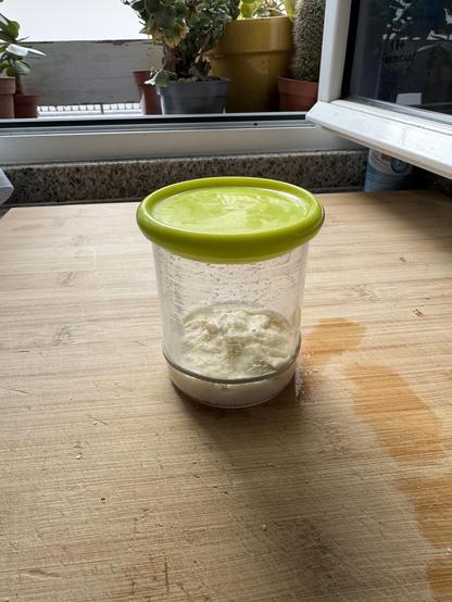 Bote de masa madre sobre una encimera donde la superficie es rugosa y hay un elástico, indicando el nivel de la masa madre
