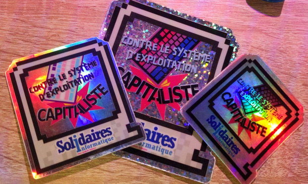 Photo de 3 stickers brillants de taille différentes avec la même forme.

Il est écrit "Contre le système d'exploitation capitaliste" avec un clavier qui casse le mot capitaliste.

L'un des sticker a un clavier aux couleurs du drapeau trans et un autre aux couleurs du drapeau bi.