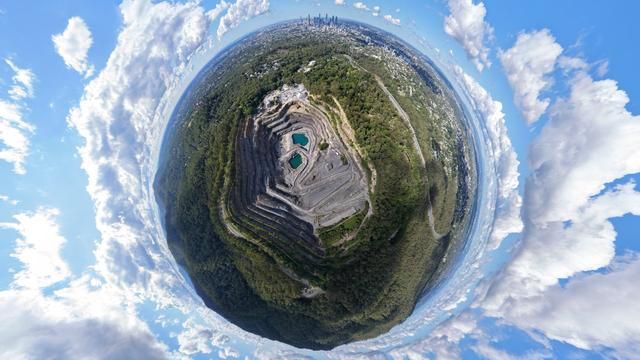 An aerial panorama of a quarry, framed to look like a small planet surrounded by clouds