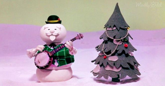 A folksy Snowman voiced by Burl Ives playing a banjo next to a Christmas tree