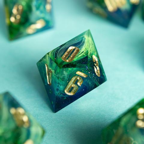 Dieser D10 zeigt einen schönen blau-grünen Verlauf mit vielen opaken swirls.

Die Zahlen sind mit gold angemalt.