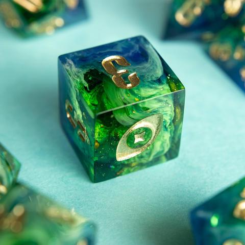 Dieser D6 zeigt einen schönen blau-grünen Verlauf mit vielen opaken swirls.

Die Zahlen sind mit gold angemalt. Die Nummer 6 wurde durch mein Logo, ein Auge mit Stern, ersetzt.