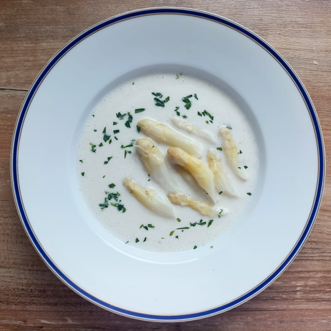 Ein Teller mit Spargelsuppe, darin 9 Spargelspitzen und fein geschnittenes Estragon