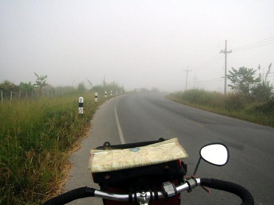 Straße im Nebel. Im Vordergund Fahrradlenker mit Landkarte, Rückspiel
