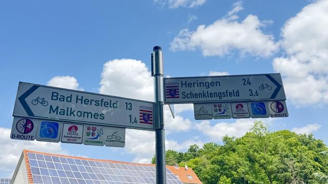 Ein Straßenschild mit Wegbeschreibungen und Entfernungen zu nahe gelegenen Orten: Bad Hersfeld (13 km), Malkomes (1,4 km), Heringen (24 km) und Schenklengsfeld (3,6 km). Es enthält Symbole für das Radfahren