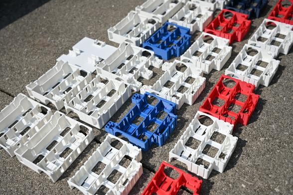 Side angle view of a variety of white, red, and blue 3D-printed iterations of the BEAPER Bot robot chassis sitting outside on grey concrete.
