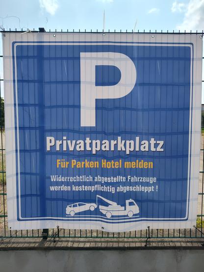 Ein Poster an einem Zaun: "P - Privatparkplatz", darunter: "Für Parken Hotel melden" [sic!]