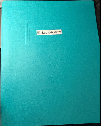 a blue-green cardstock paper folder with a printed label that reads "6581 Sound Interface Device"