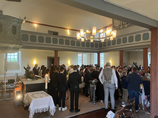 Im Kirchenraum, viele Menschen stehen redent herum und schauen durch die geöffnete Tür auf den Regen.