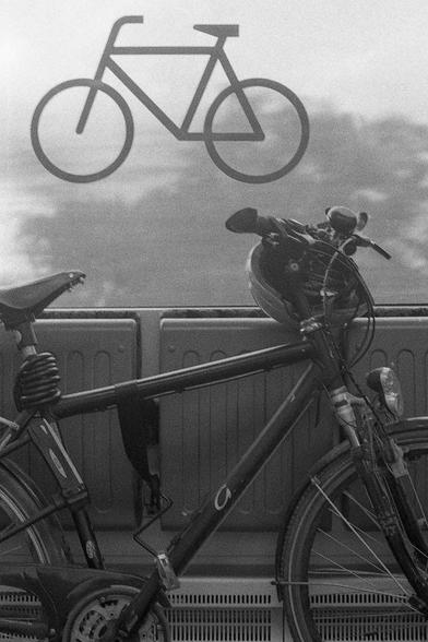 Das Schwarzweißbild zeigt ein Fahrrad, das in einem Zug abgestellt ist, mit einem Fahrrad-Piktogramm an der Fensterscheibe im Hintergrund.