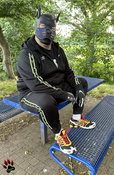 human pup wearing a Nike tracksuit, Nike football gloves, white socks and Nike Shox sneakers sitting on a table at a German motorway rest area, looking into the camera