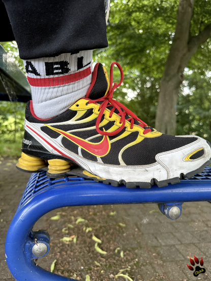 closeup on a Nike Shox ID-sneaker in black/yellow/red colourscheme set down on metal frame bench
