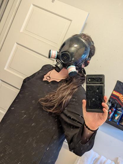 Mirror selfie of Nyxie in a black dress with MSA millennium gasmask and trans colored filters.