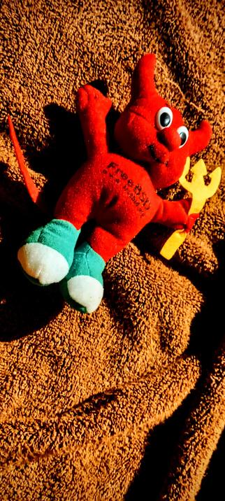 The photograph composed in total darkness, warmed up with a 81A filter features a red plush toy resembling a devil, the freeBSD mascot, lying on a brown textured surface. The toy has large, googly eyes, a small nose, and a smiling mouth. It is wearing teal socks with white toes and has a lovely red tail. The toy is holding a yellow trident in its right hand. The text "freeBSD" is printed on its chest. The plush toy is positioned with its arms spread out, giving it a relaxed appearance. The background is a brown, fuzzy fabric, possibly a towel or blanket, with shadows cast by the toy, adding depth to the image.

 Ovis2-8B

🌱 Energy used: 0.185 Wh