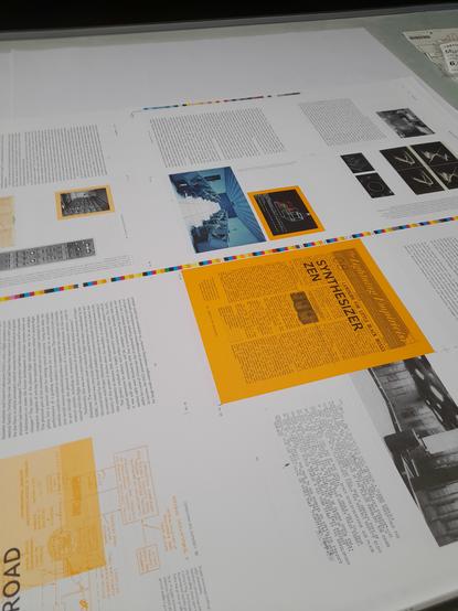A surface with a large sheet of paper containing multiple pages. Several historical images in black and white are visible, one in colour, one page stands out among the others because it has a bright orange-yellow background, with the chapter title 'Synthesizer Zen'.
