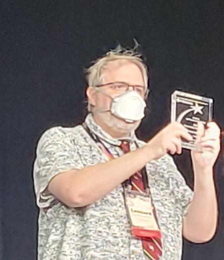 Leonard on stage, holding up a rectangular glass object (the award)