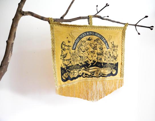 Etendard rectangulaire couleur moutarde avec illustration en noir et franges dorées : une une farandole dionysiaque de bêtes dansant et jouant du tambourin et de la double-flute dans les narines. Il y a un cochon, une grenouille démesurée, un lievre, un bouc et un-e démon-e ayant des yeux à la place des coudes et des bouches à la place des genoux. Entre ces bestioles, un figuier et une vigne enfoncent leurs racines dans le sol, racines qui ont poussées sur les squelettes de chefs militaires, politiques et d'homme d'affaire : on voit le sous-sol en coupe. Un serpent est enroulé autour d'un squelette et s'écrit dans une bulle "Compost the capitalist and fascist scum!"