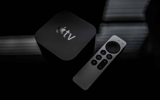 Dunkle S/W-Aufnahme von einem schwarzen Apple TV und einer silbrig-glänzenden Apple Remote auf einer leicht spiegelnden Oberfläche.