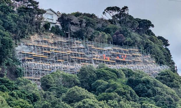 Huge scaffolding setup on a hill side with several tiny workers in high viz.